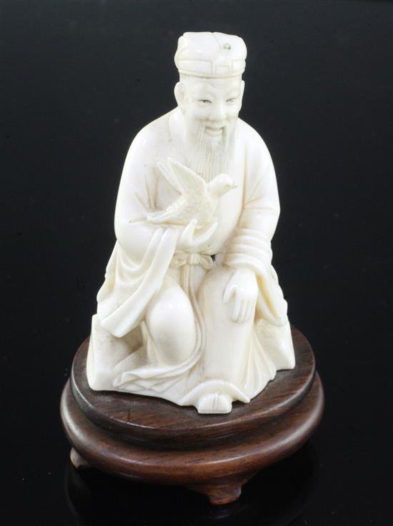 A Chinese ivory seated figure of a scholar holding a bird, early 20th century, wood stand, total height, 10cm